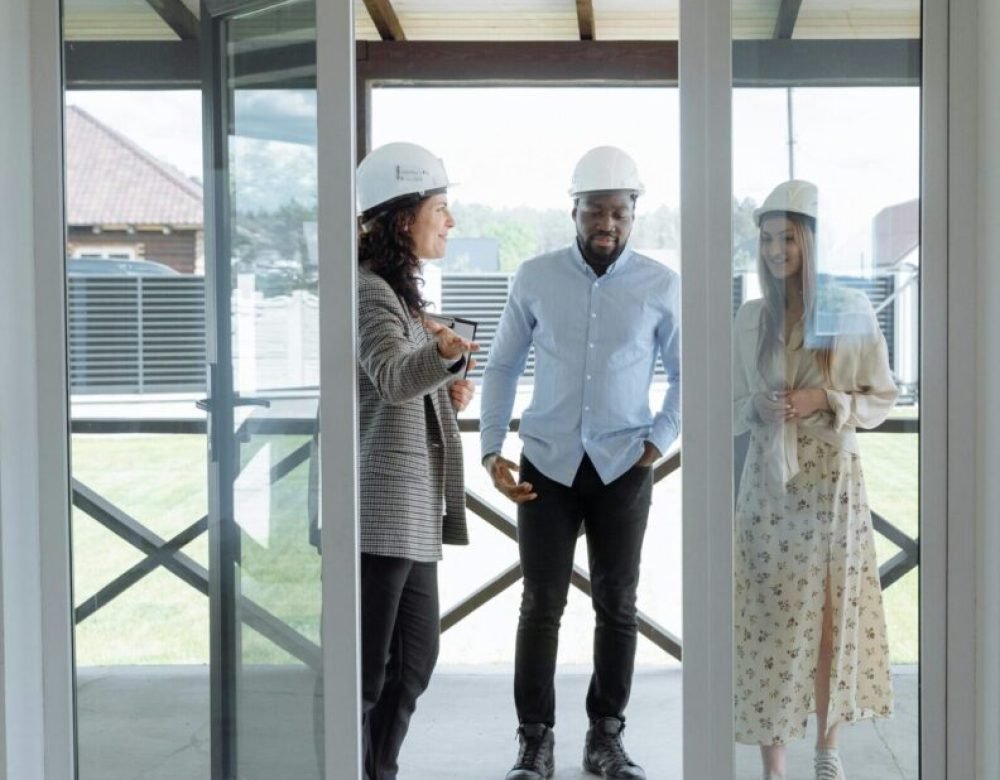 pexels-photo-8469997-8469997 Three real estate professionals in hard hats discussing home features during a house tour.